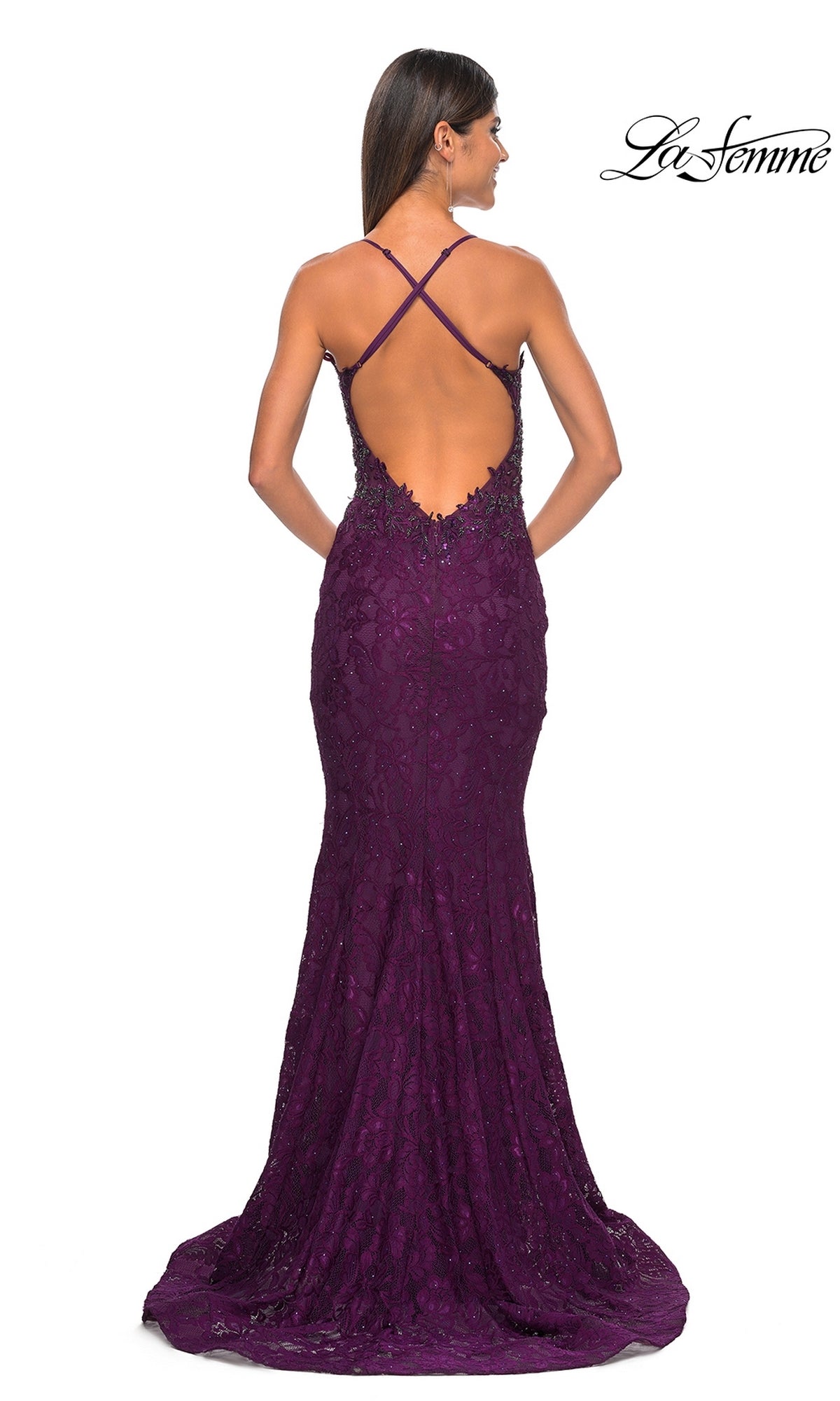 A woman stands with her back to the camera in the La Femme Beaded-Lace Long Prom Dress 31265, a deep purple fitted mermaid gown featuring beaded lace, a low open back with crisscross straps, and a slight train.